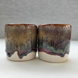 set of two handmade ceramic cups with a warm amber glaze blending into brown, maroon and green tones over a warm white base