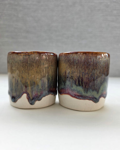 set of two handmade ceramic cups with a warm amber glaze blending into brown, maroon and green tones over a warm white base