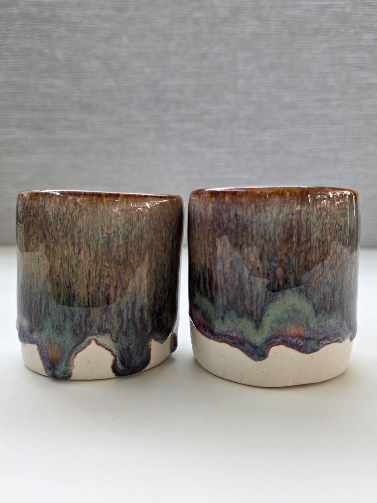 set of two handmade ceramic cups with a warm amber glaze blending into brown, maroon and green tones over a warm white base