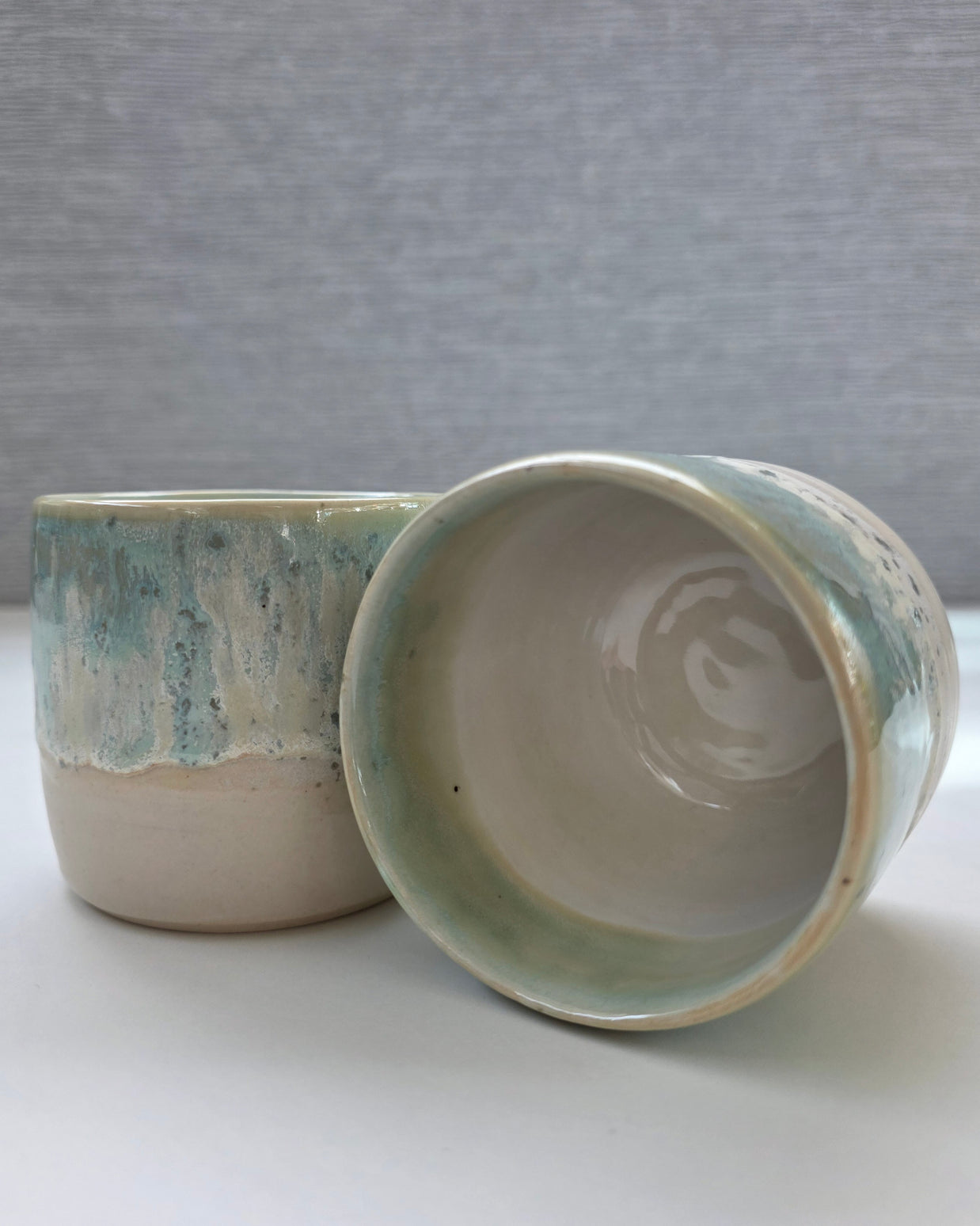 set of two handmade ceramic cups featuring a white interior with blue-green rim detailing