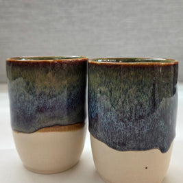 set of two handmade ceramic cups with glaze blending green, brown, blue, and amber tones over a warm white base