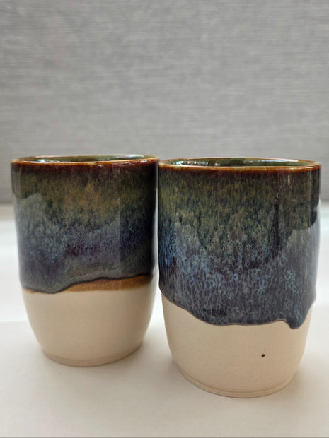 set of two handmade ceramic cups with glaze blending green, brown, blue, and amber tones over a warm white base