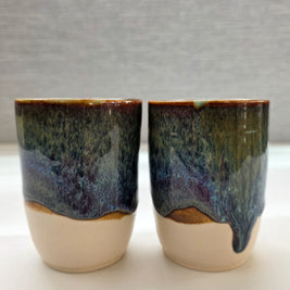 set of two handmade ceramic cups with glaze blending green, brown, blue, and amber tones over a warm white base