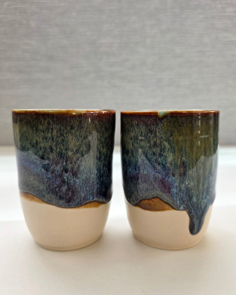 set of two handmade ceramic cups with glaze blending green, brown, blue, and amber tones over a warm white base