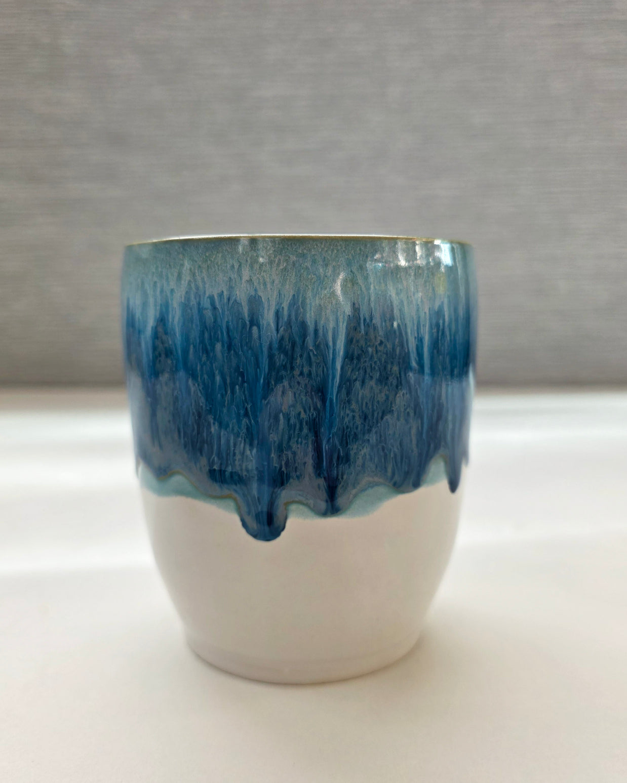 handmade ceramic cup with blue dripping glaze over a white base