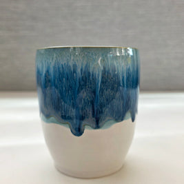 handmade ceramic cup with blue dripping glaze over a white base