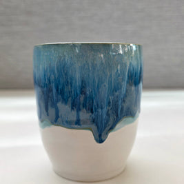 handmade ceramic cup with blue dripping glaze over a white base