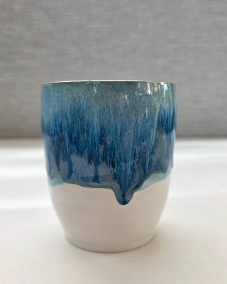 handmade ceramic cup with blue dripping glaze over a white base