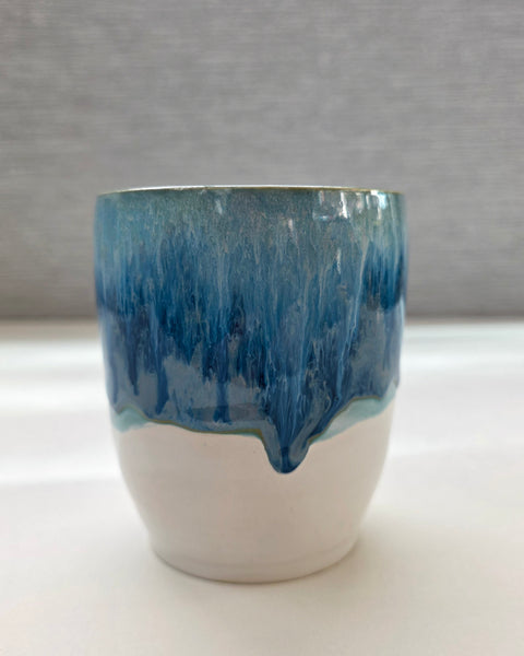 handmade ceramic cup with blue dripping glaze over a white base