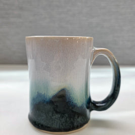 handmade ceramic mug with a handle, finished in a soft gradient glaze transitioning from warm white to a deep teal base