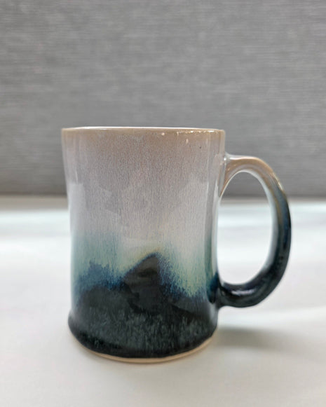 handmade ceramic mug with a handle, finished in a soft gradient glaze transitioning from warm white to a deep teal base