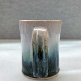 handmade ceramic mug with a handle, finished in a soft gradient glaze transitioning from warm white to a deep teal base