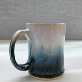 handmade ceramic mug with a handle, finished in a soft gradient glaze transitioning from warm white to a deep teal base