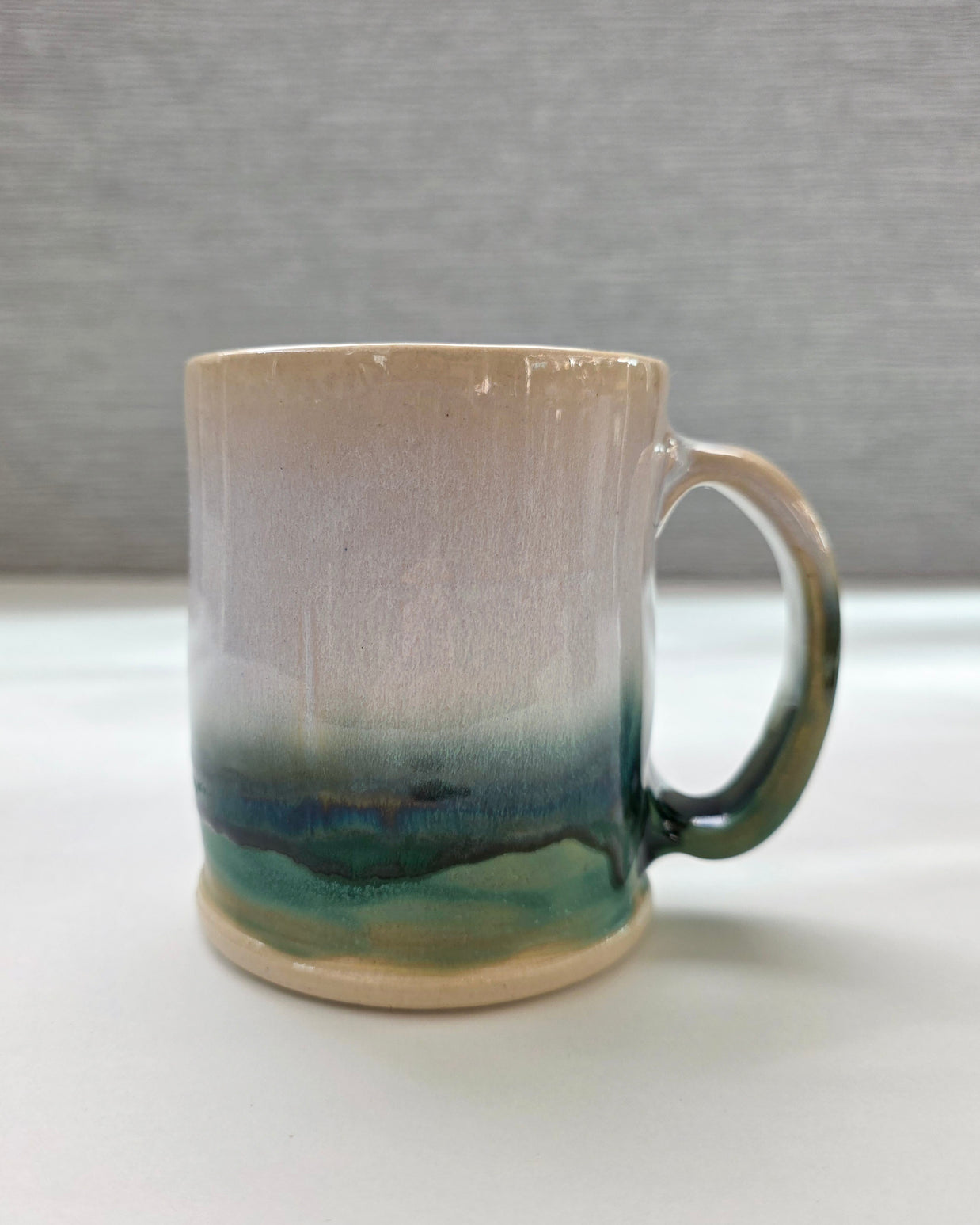 handmade ceramic mug with a handle, finished in a soft gradient glaze transitioning from warm white to a deep green base