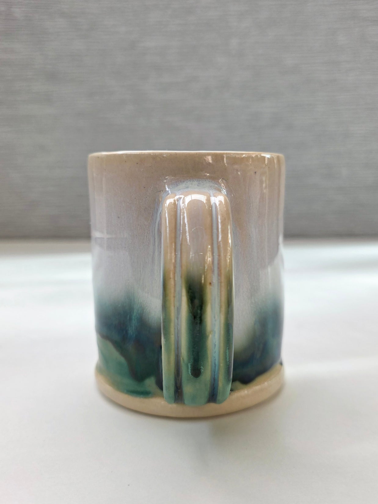 handmade ceramic mug with a handle, finished in a soft gradient glaze transitioning from warm white to a deep green base