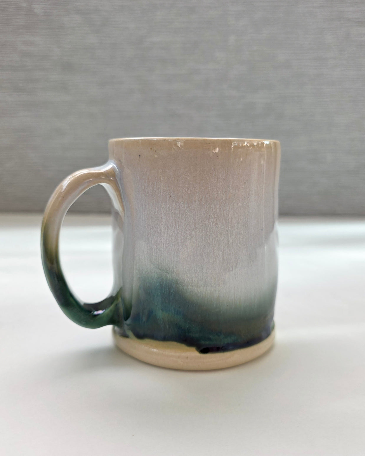 handmade ceramic mug with a handle, finished in a soft gradient glaze transitioning from warm white to a deep green base