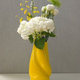 a bright yellow sculptural ceramic vase filled with flowers