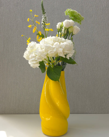a bright yellow sculptural ceramic vase filled with flowers