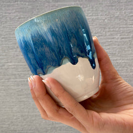handmade ceramic cup with blue dripping glaze over a white base