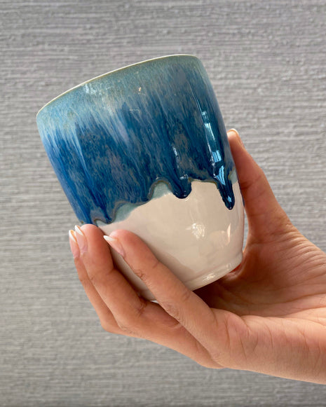 handmade ceramic cup with blue dripping glaze over a white base